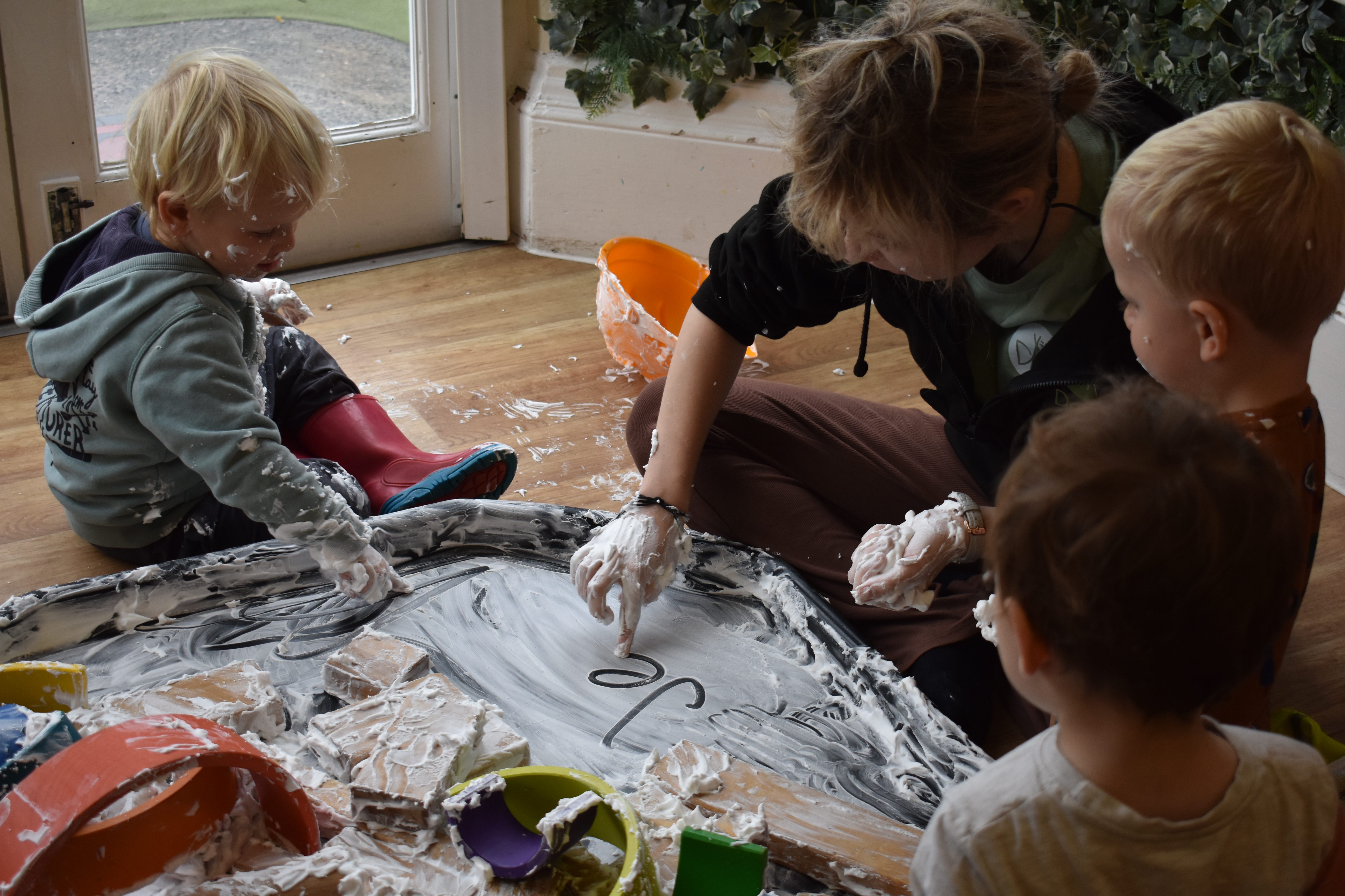 Children sat in a circle with a nursery leader at Devon Nurseries painting