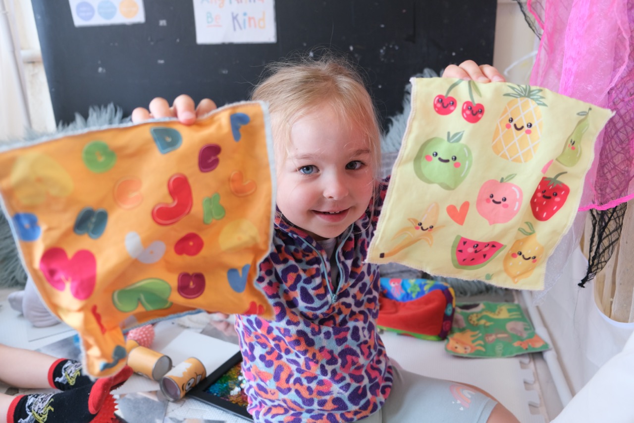 A child at Devon Nurseries playing with coloured and patterned sheets